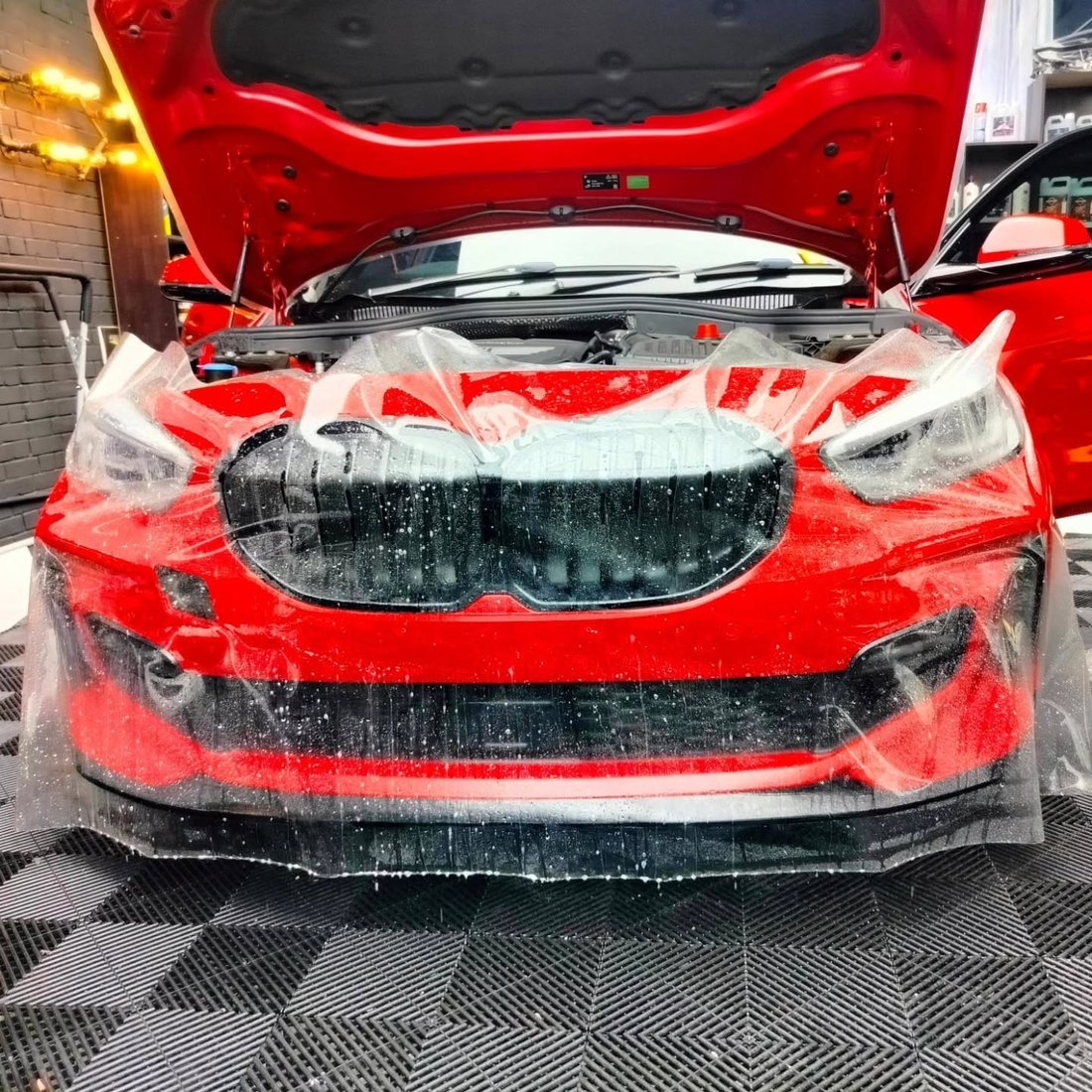Paint protection film being applied to the front bumper and grille of a red BMW with the bonnet open
