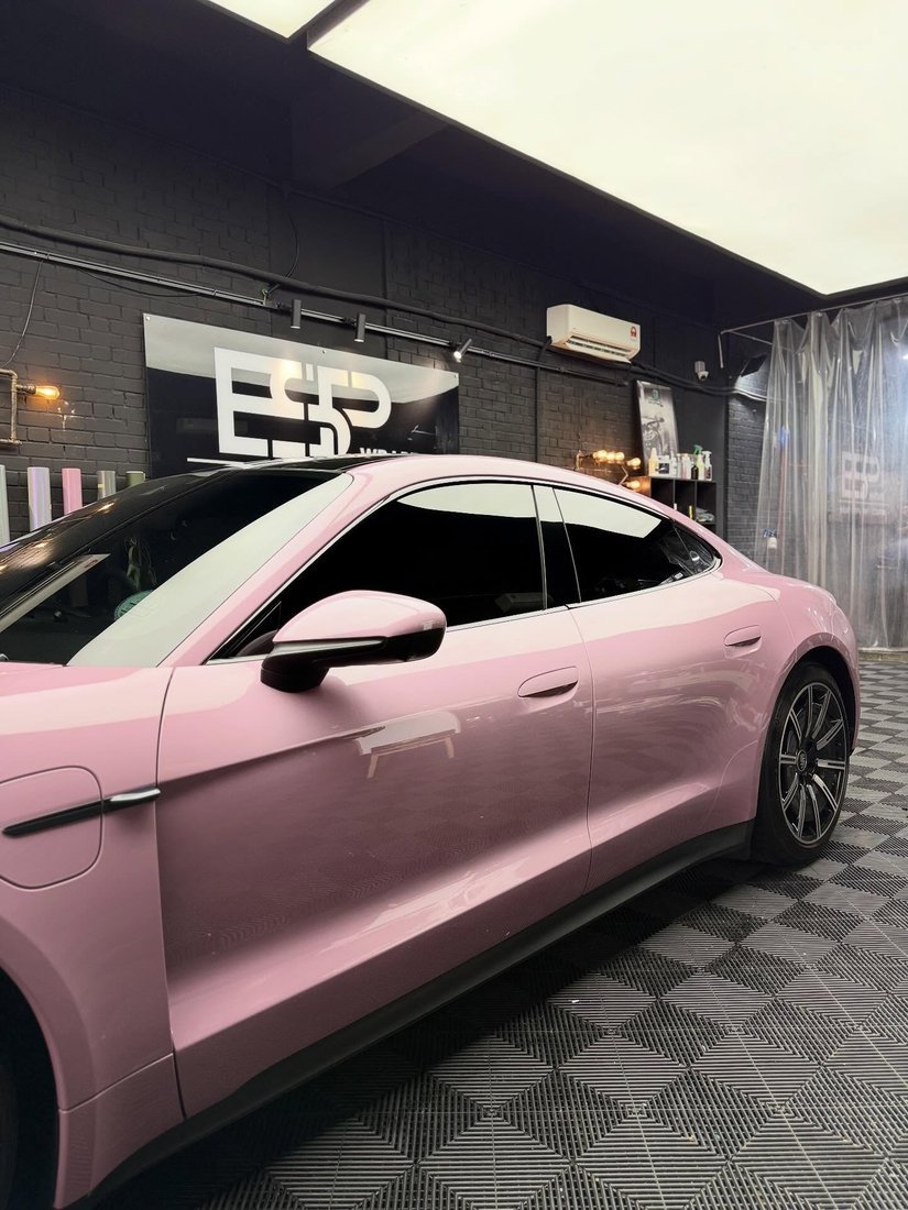 A Porsche Taycan finished in pink colour-tinted paint protection film with tinted side windows, front three-quarter view