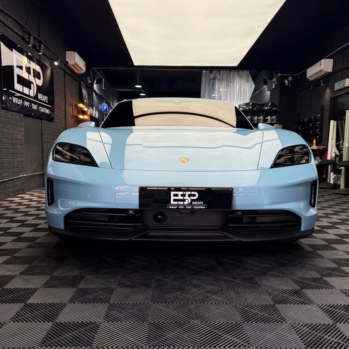 A powder-blue Porsche Taycan, front view, inside the ESP Wrapz workshop