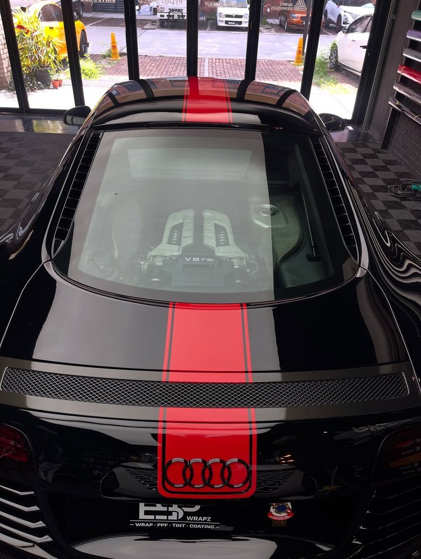 A black Audi R8 with a red racing stripe wrap, top-down rear view showing the V8 engine through the glass