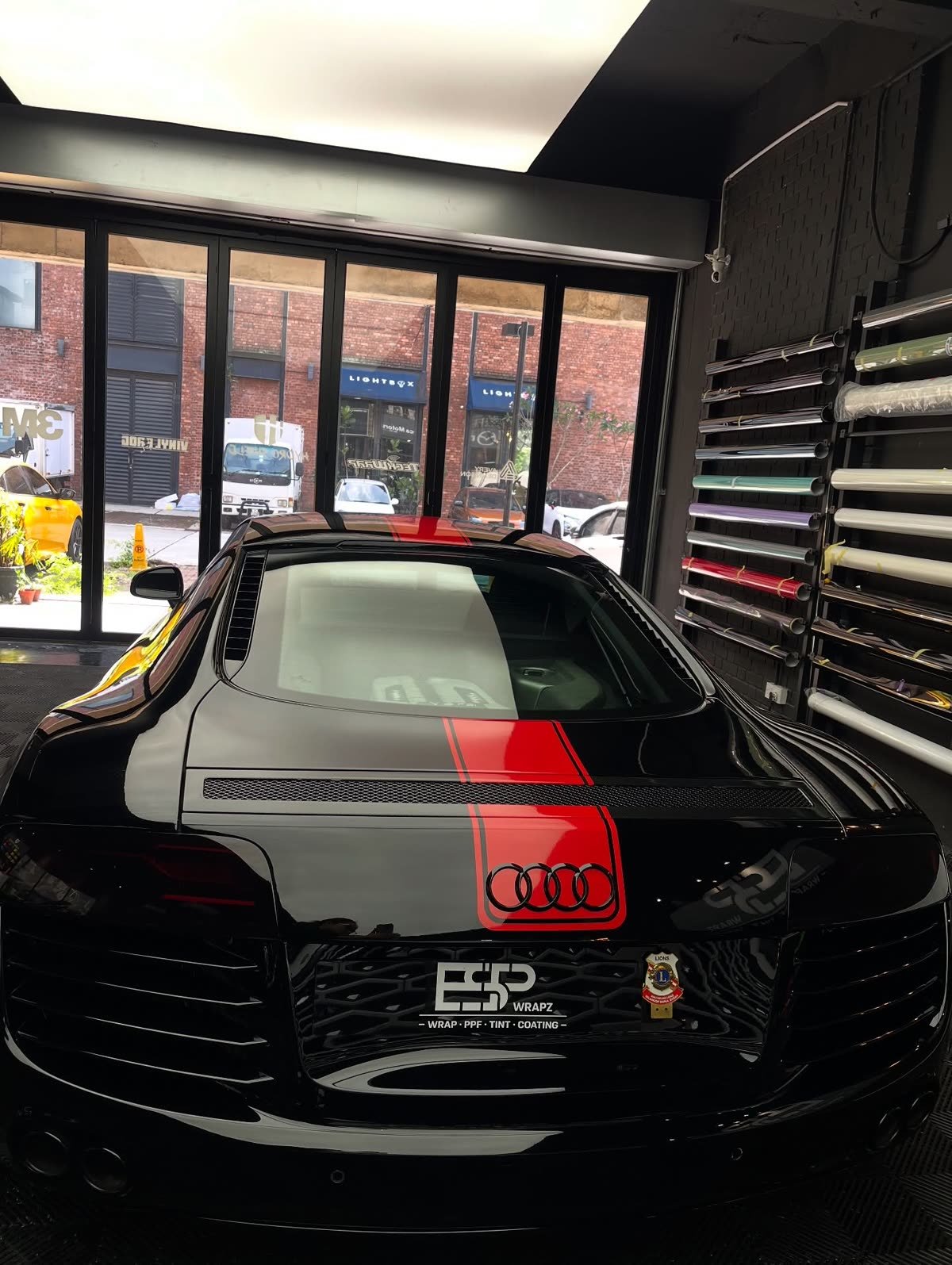 A black Audi R8 with a red and grey racing stripe colour wrap, wide rear view of the ESP Wrapz workshop