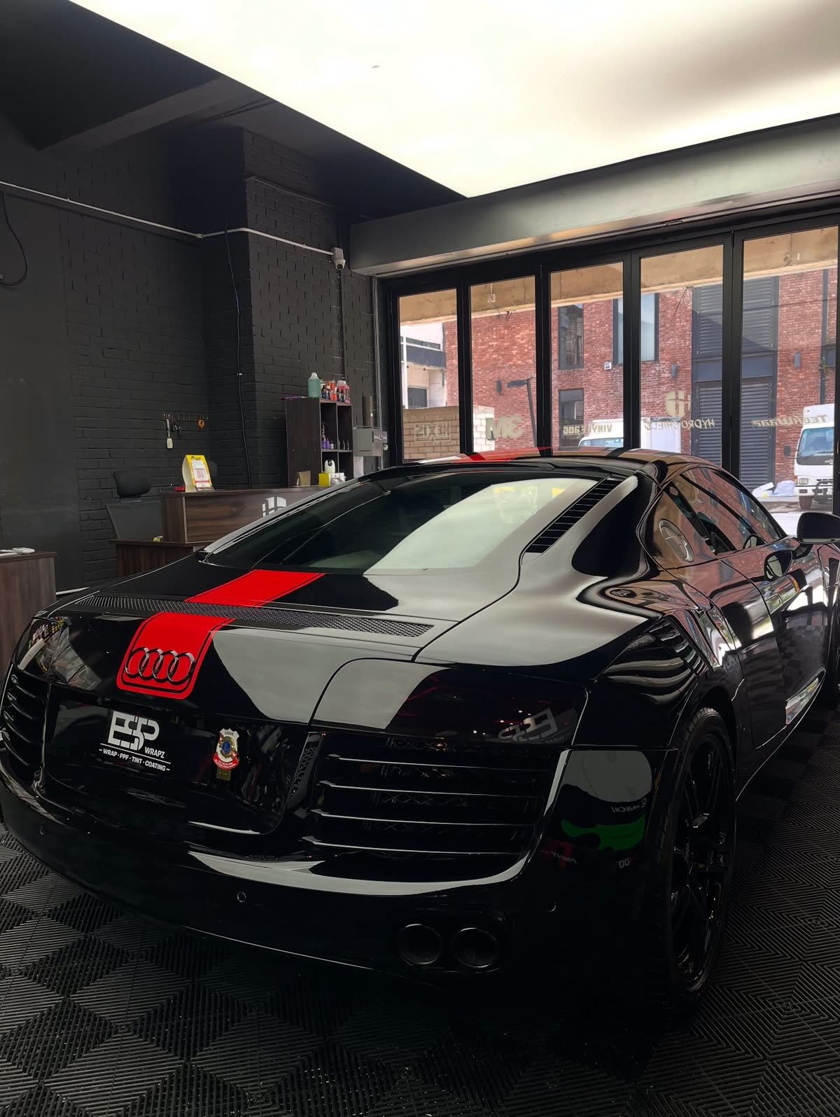 A black Audi R8 with a red racing stripe wrap, rear three-quarter view with the ESP Wrapz office visible