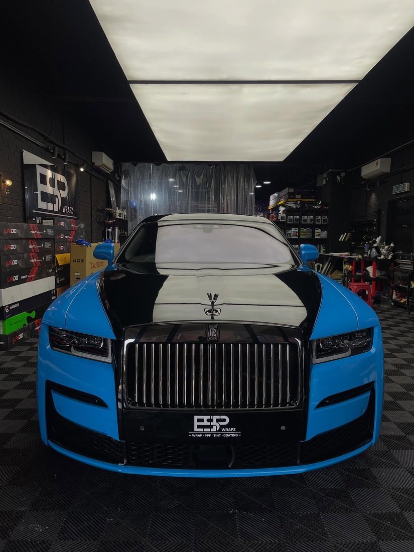 A Rolls-Royce Ghost with a two-tone sky blue and black colour wrap, straight-on front view showing the grille